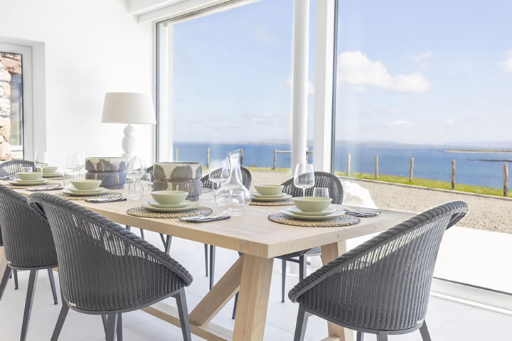 Dining table at Golden Strand View holiday home, with full height glass wall overlooking Golden Strand beach
